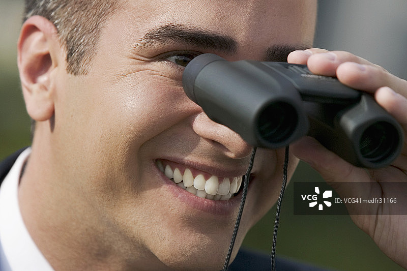 微笑的商务人士使用双筒望远镜的特写镜头图片素材