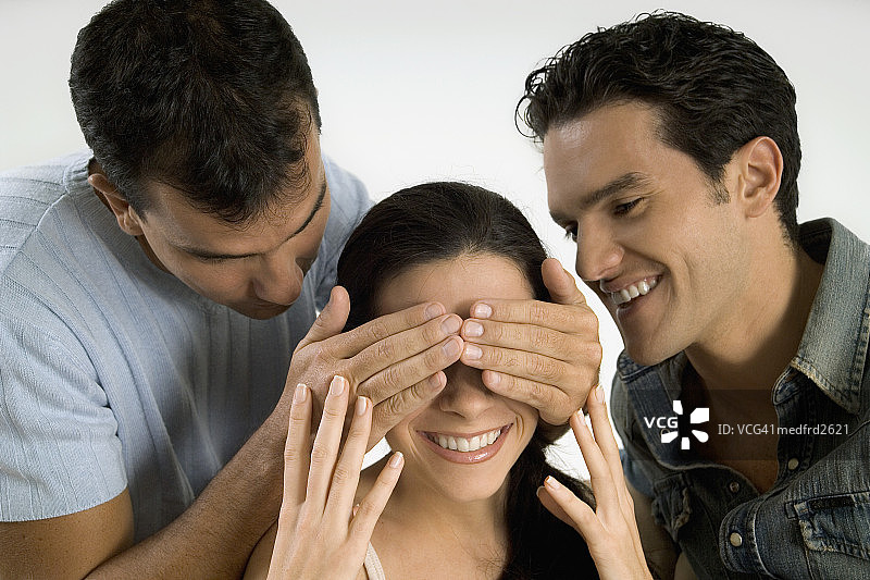 男人蒙住微笑女人的眼睛，另一个男人看着她，特写图片素材