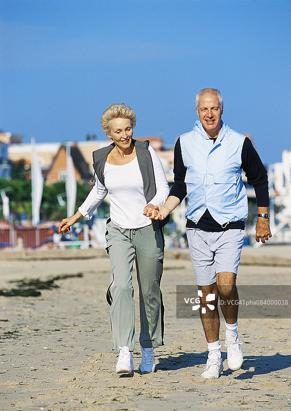 老年夫妇手牵手在沙滩上散步图片素材