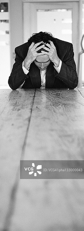 黑白照片：坐在桌旁用手捂头的商人图片素材