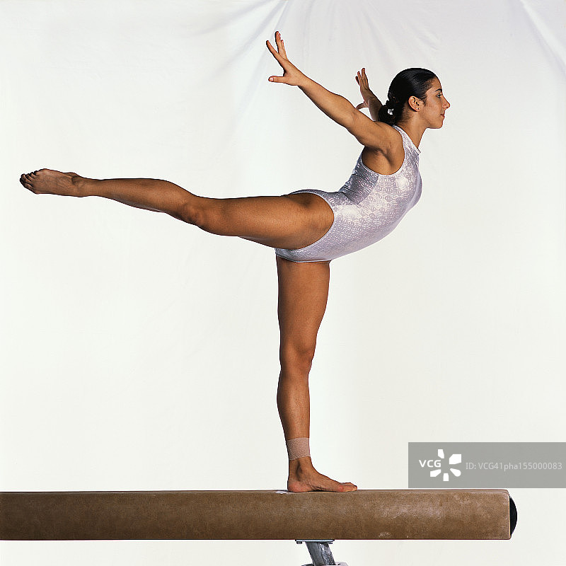 年轻女体操运动员在平衡木上做练习图片素材