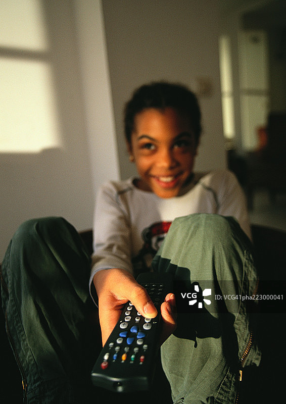 小男孩坐在那里，用遥控器指着电视，微笑着图片素材