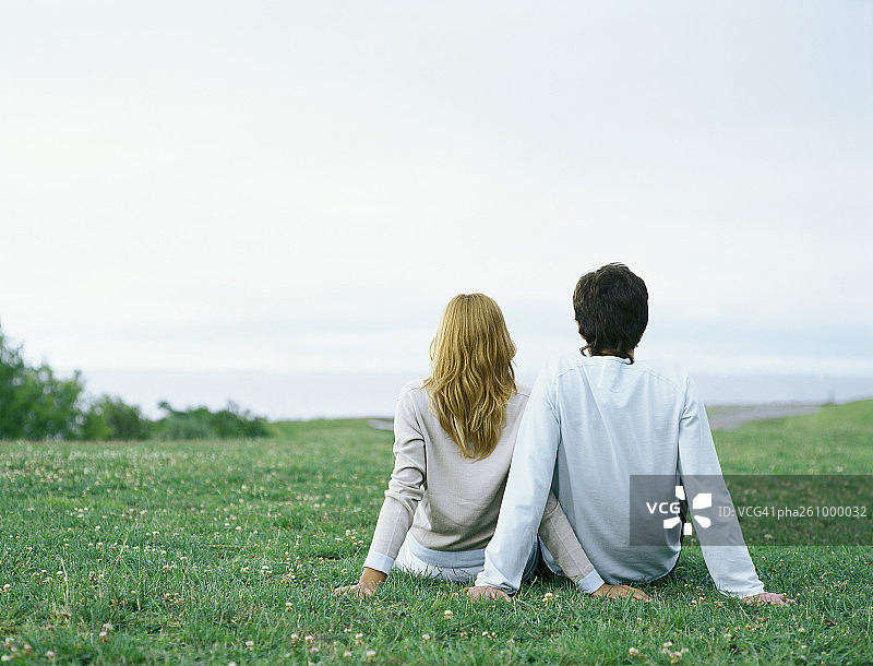 年轻男人和年轻女人并排坐在草地上，用手支撑着，后视图图片素材