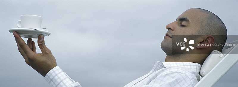 男人仰着头闭着眼睛，用指尖平衡着杯碟图片素材