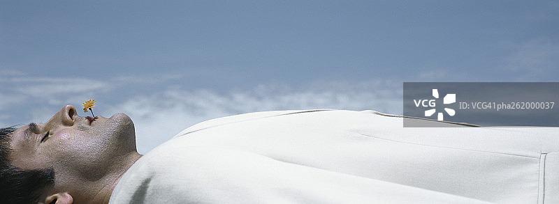 男子仰卧，嘴里含着花，背景是天空，特写镜头图片素材