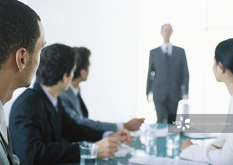 商务人士在桌边就座，看向背景中带背光的商人图片素材