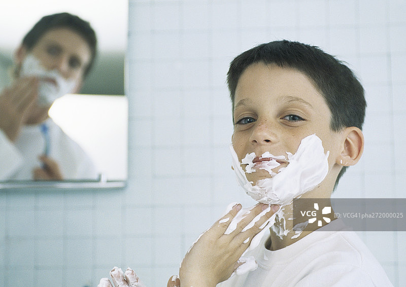 脸上和手上涂满剃须膏的男孩，背景是正在刮胡子的男人图片素材