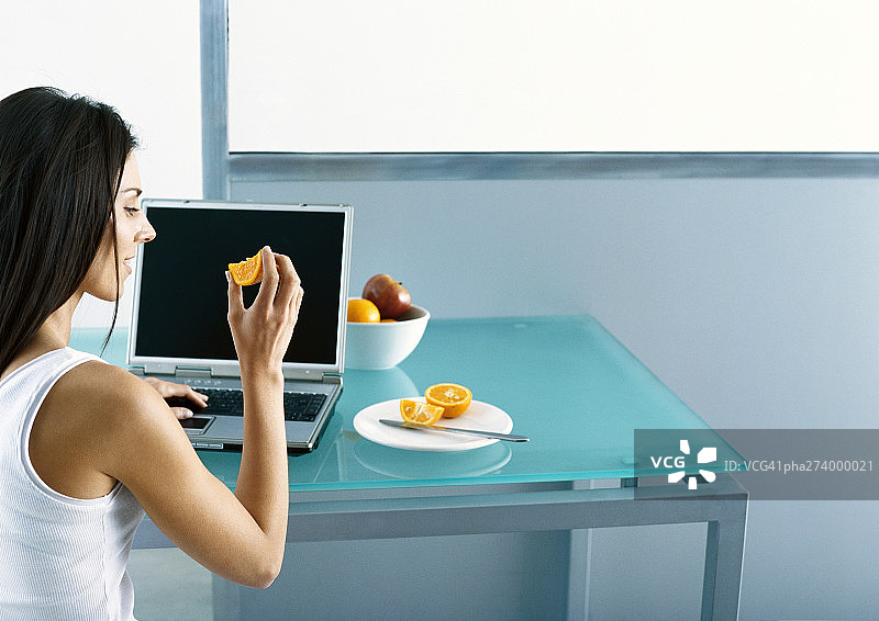 在桌旁用笔记本电脑吃水果的女人图片素材