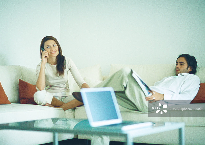 男人和女人坐在沙发上，男人在阅读，女人在使用手机图片素材