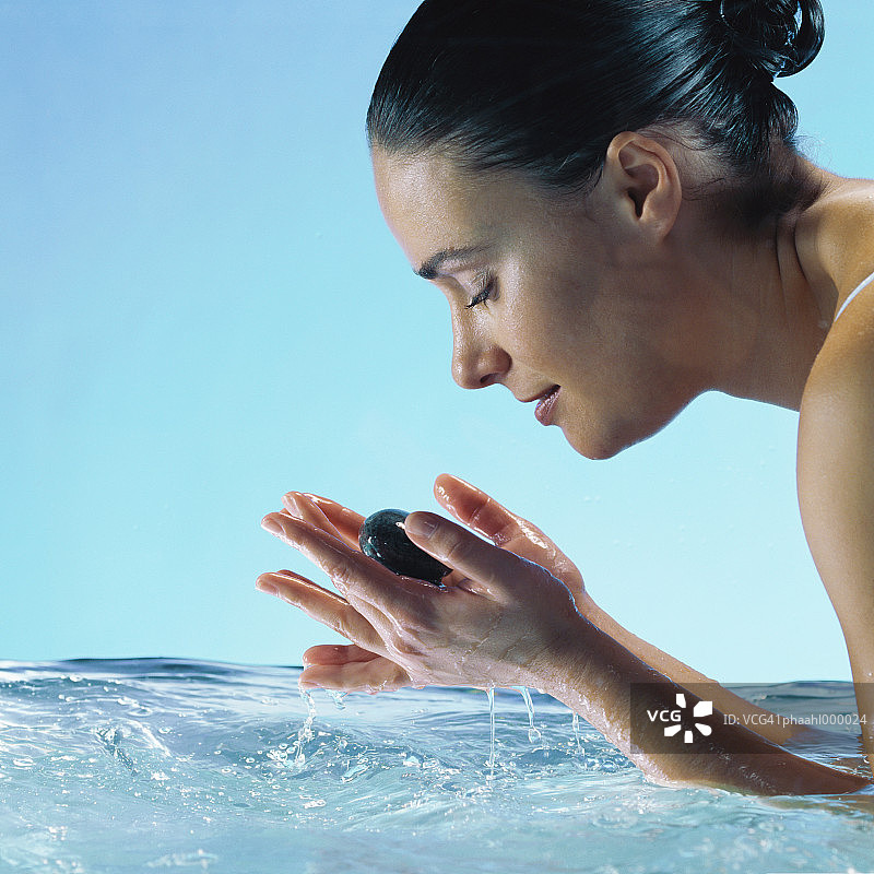 在水中闭着眼睛、手持石头的女人（侧视图）图片素材