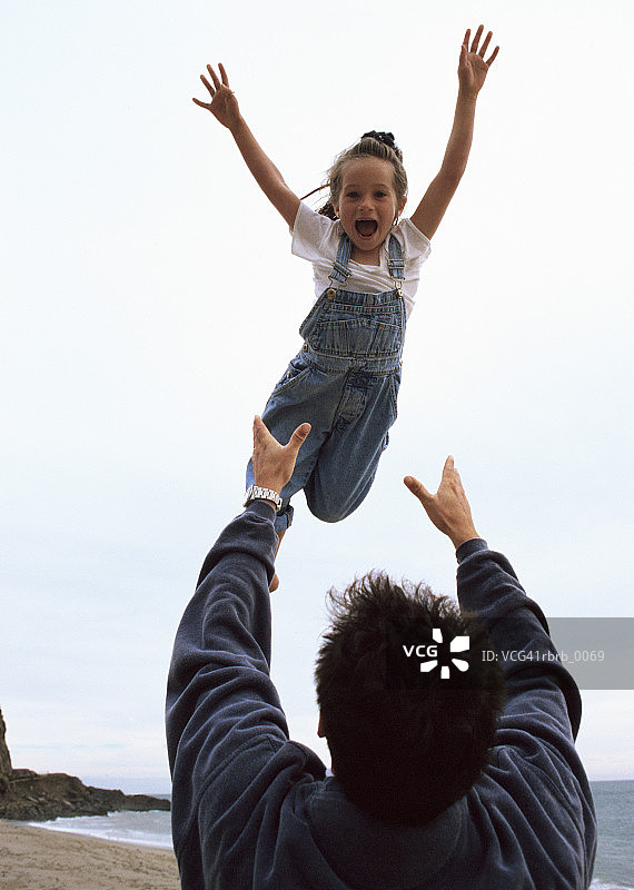 白人父亲在海滩上将笑着的女儿抛向空中图片素材