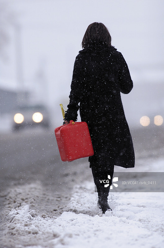 一名白人女性在雪中拿着汽油罐走在路上的生活照图片素材
