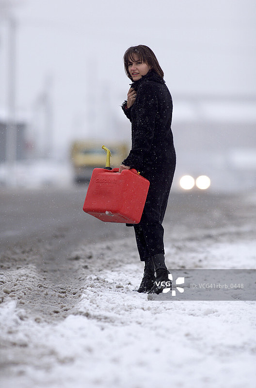 雪天：白人女性提着汽油罐在路边图片素材