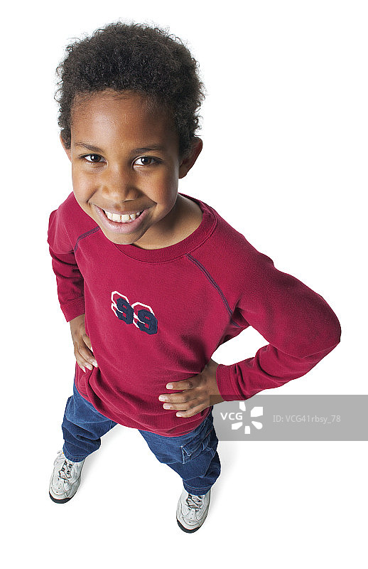 穿着牛仔裤和红色衬衫的年轻非裔美国男孩双手叉腰，对着镜头微笑图片素材