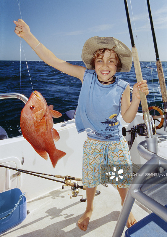 站在船上拿着鱼微笑的男孩（8-9岁）肖像图片素材