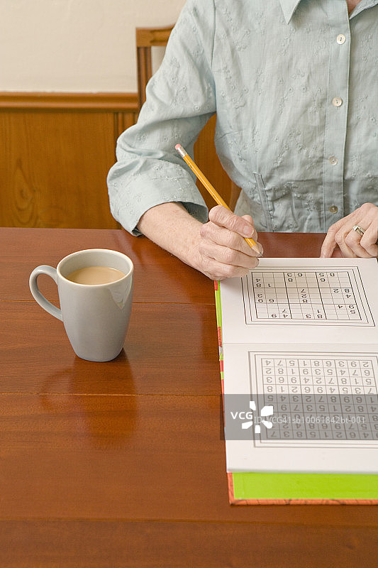 年长的女人坐在桌旁玩数独，中段视角图片素材
