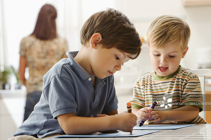 两名（3-7岁）男孩在桌子上画画，母亲在背景中图片素材