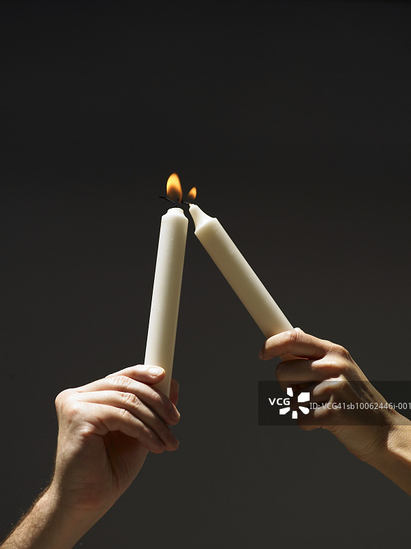 手持点燃的蜡烛，另一个人试图点燃另一根蜡烛，手部特写图片素材