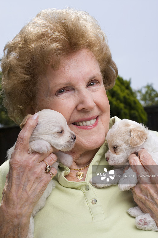 年长的女人抱着两只小狗，笑着，户外，肖像图片素材