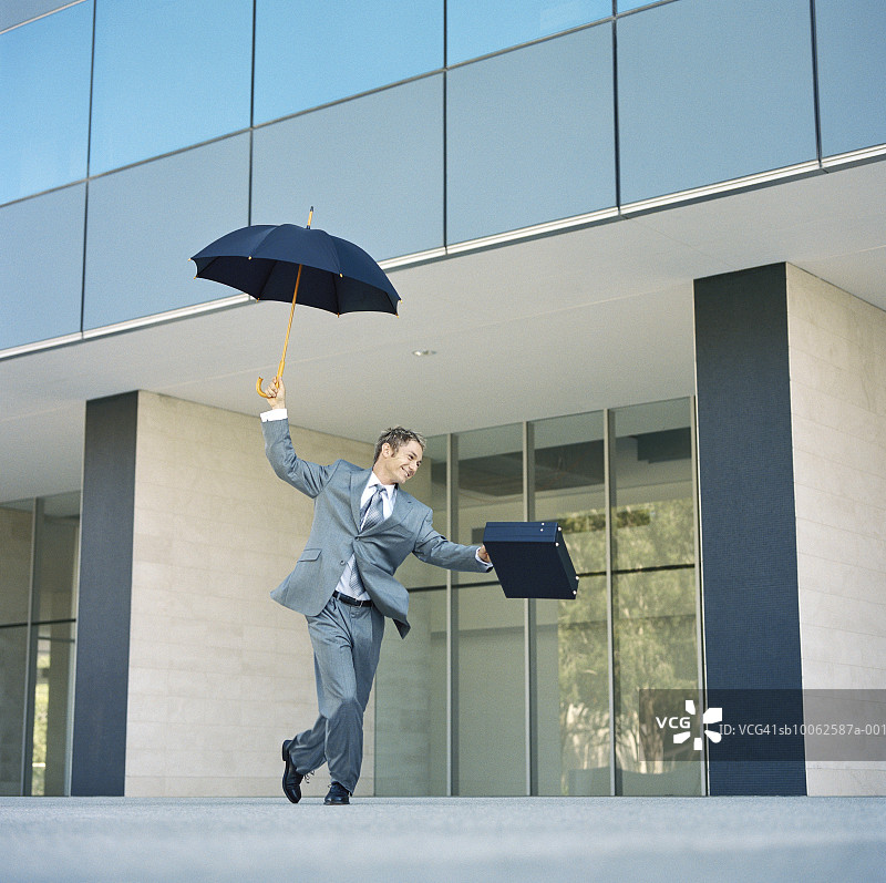 在办公楼前打着雨伞跳舞的商务人士图片素材