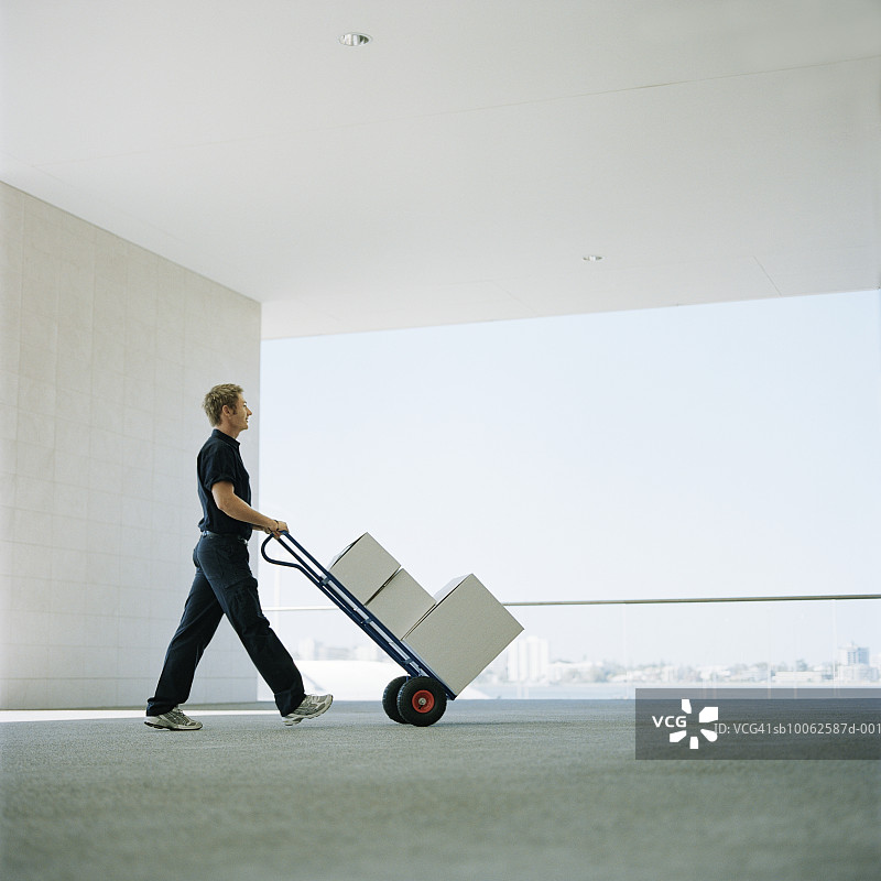 快递员在户外用手推车搬运箱子，侧视图图片素材