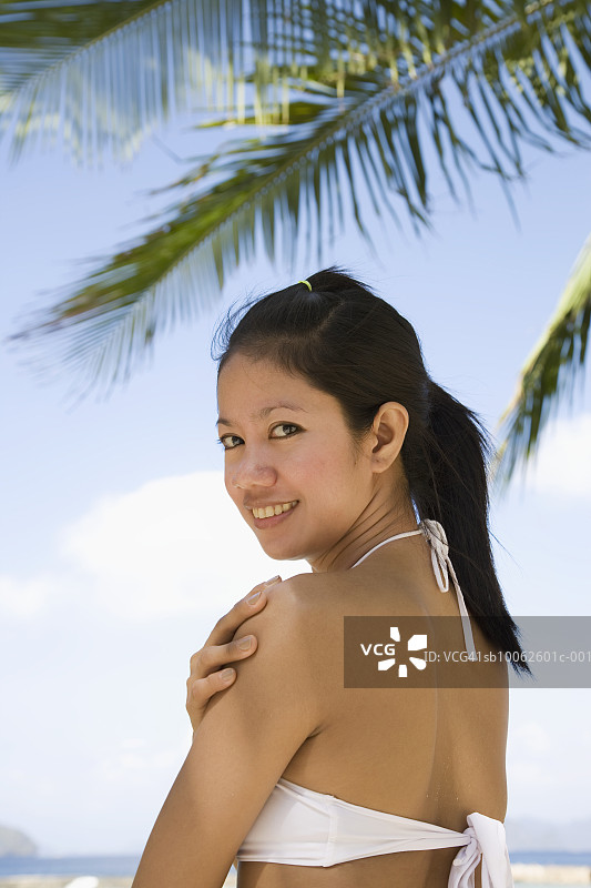 在海滩上，回头微笑的年轻女人肖像图片素材