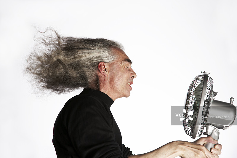 中年男人拿着电风扇对着脸，侧视图图片素材