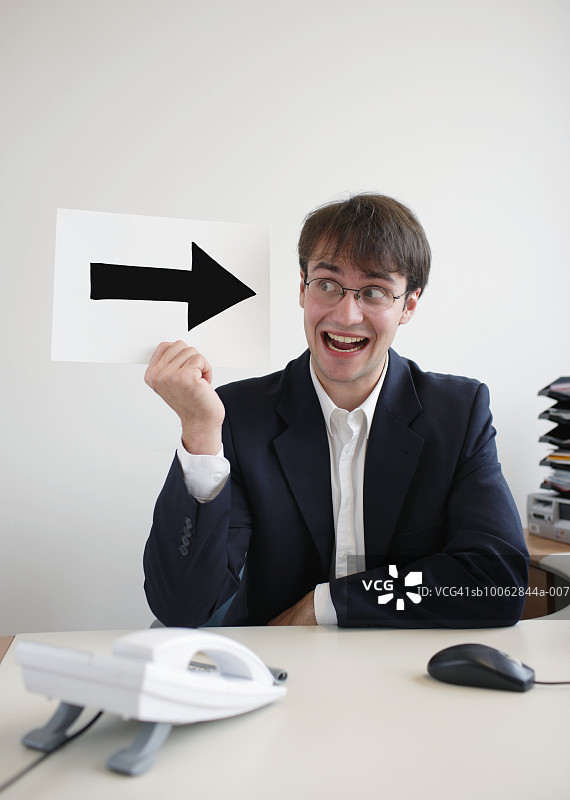 在办公桌旁拿着纸箭微笑的商人图片素材