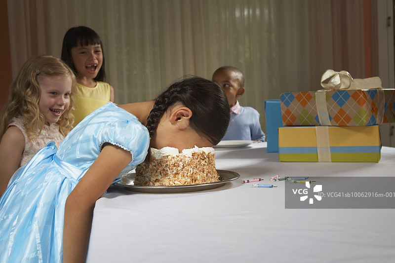 四个孩子（5-8岁）在桌旁，笑着看脸上沾满蛋糕的女孩图片素材