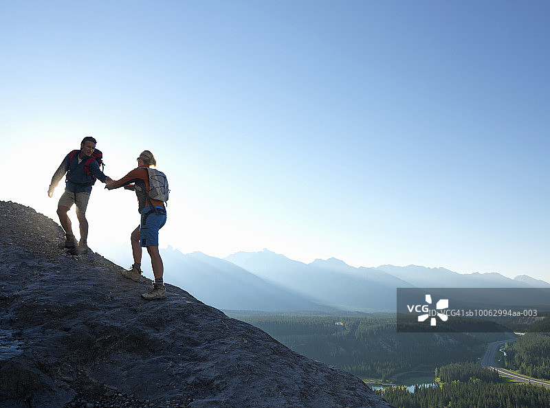 男人在山中岩脊上帮助女人图片素材