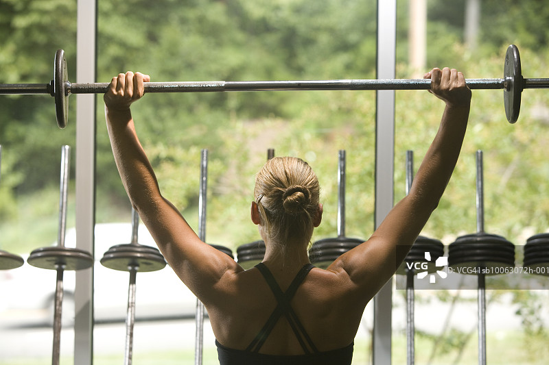 年轻女人用杠铃锻炼，后视图图片素材
