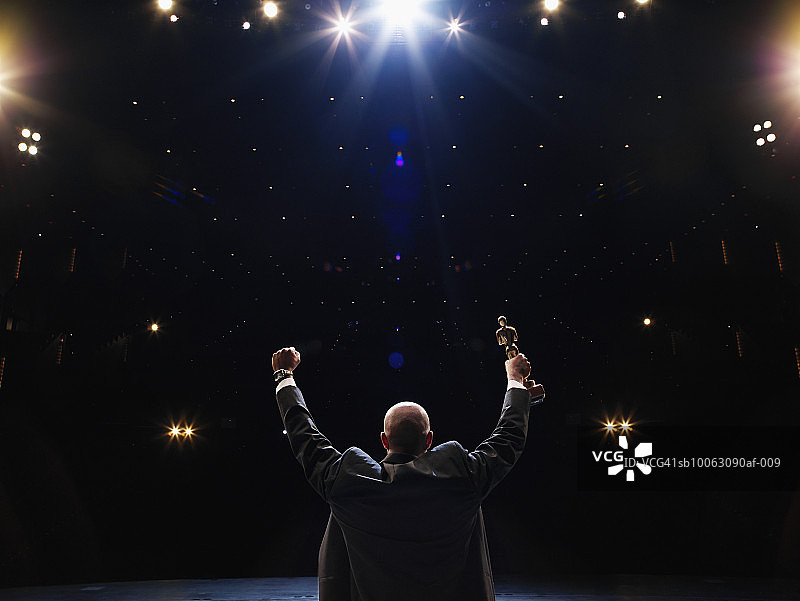 男人举着奖杯面向观众，后视图图片素材