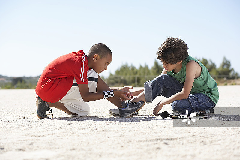 两个男孩（9-11岁）蹲在沙滩上系鞋带图片素材