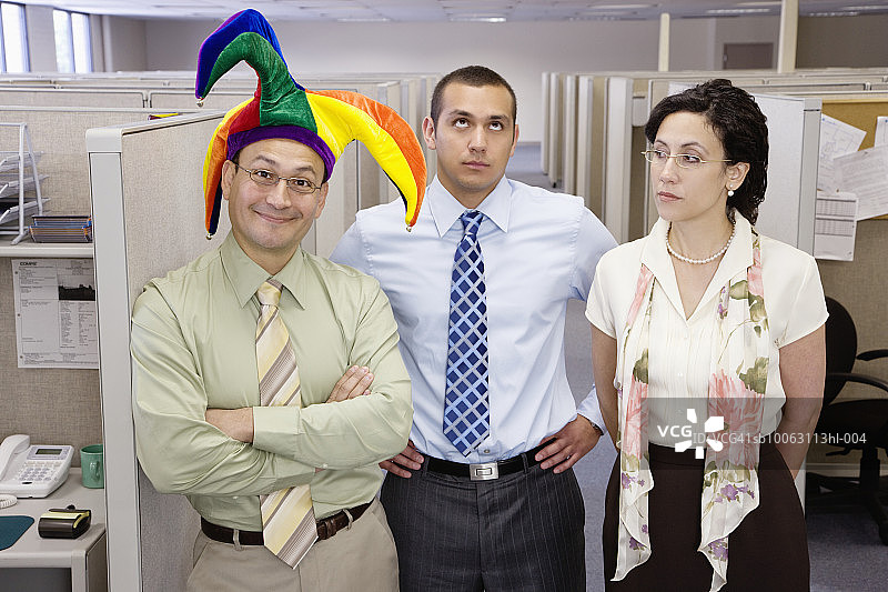 办公室隔间旁的三位同事，男子头戴小丑帽图片素材
