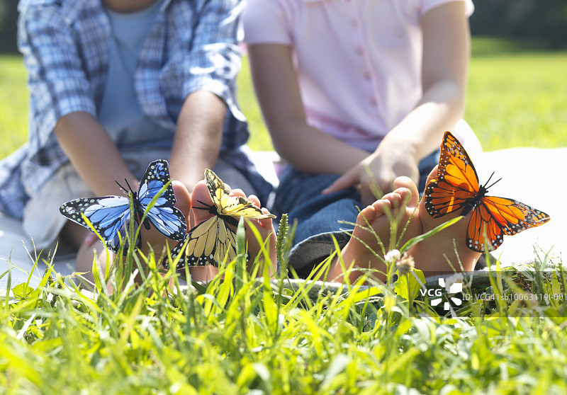 哥哥和妹妹（4-7岁）坐在草地上，脚上有蝴蝶图片素材