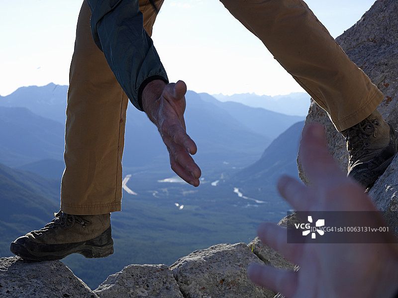 男人帮助女人攀登高峰，手部特写，背景为山谷图片素材