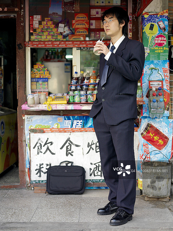 中国北京：在信息亭前饮用的年轻商人图片素材