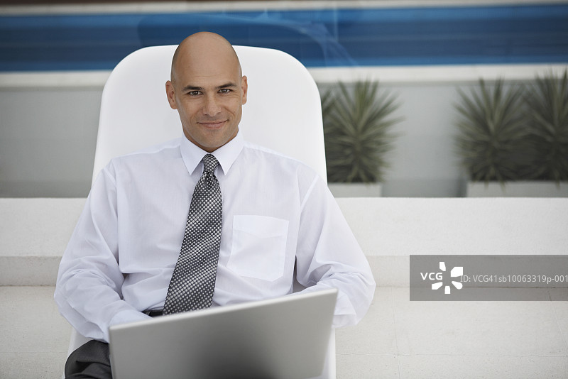 坐在躺椅上使用笔记本电脑微笑的商人肖像图片素材