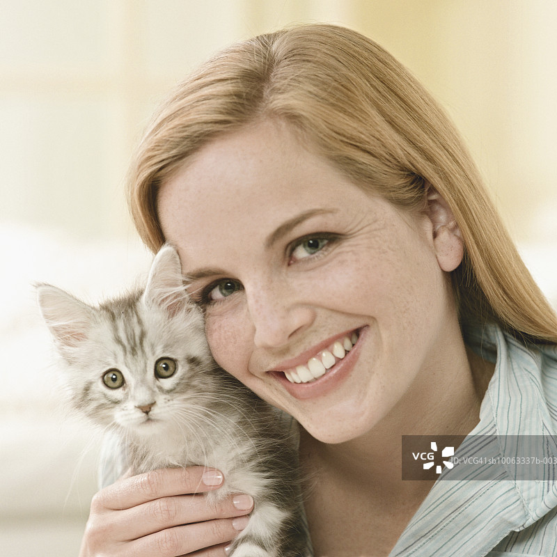 年轻女人抱着缅因猫小猫，面带微笑图片素材