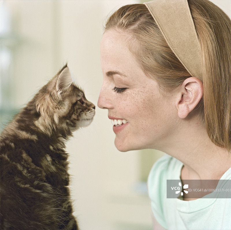 年轻女人和缅因猫小猫碰鼻子特写图片素材