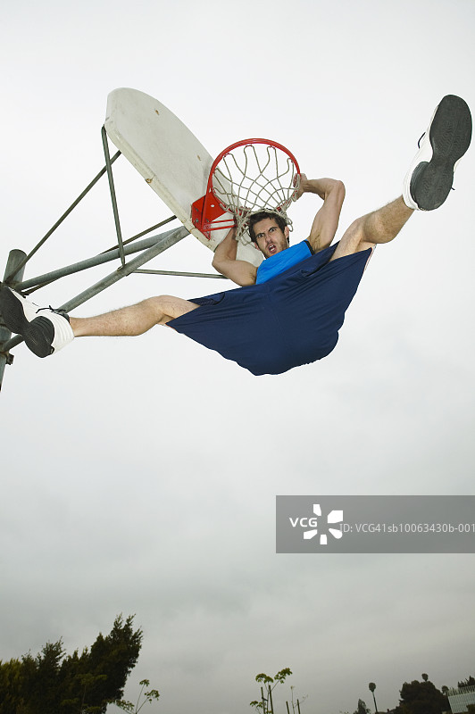 低角度拍摄的悬挂在篮球框上的年轻人图片素材