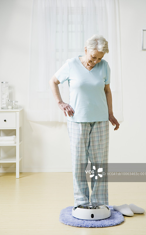 老年妇女在家中站在浴室磅秤上图片素材