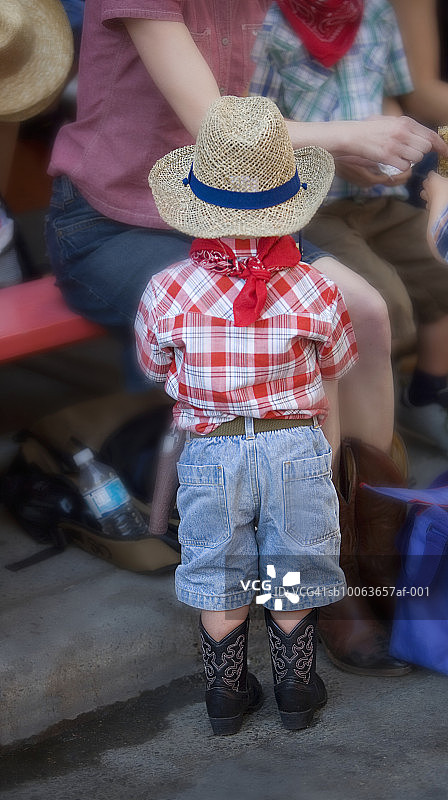 穿着牛仔服站在卡尔加里牛仔节游行队伍中的男孩（后视图）图片素材