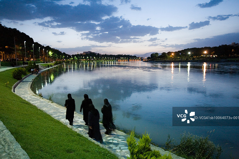 伊朗伊斯法罕，穿着罩袍的妇女傍晚沿扎因代河行走图片素材