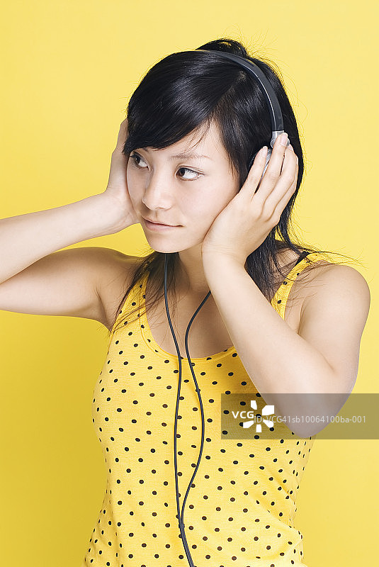 黄色背景下的戴耳机年轻女人图片素材