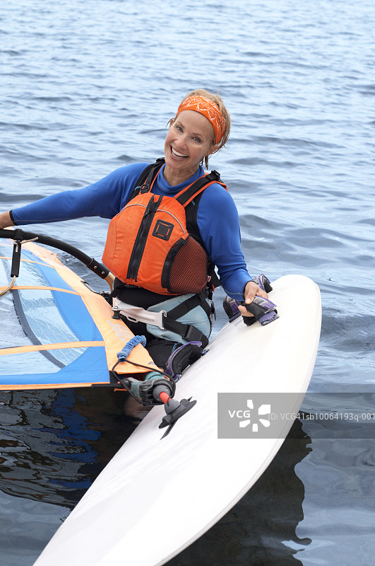 中年妇女在湖边拿着帆板微笑，肖像照图片素材