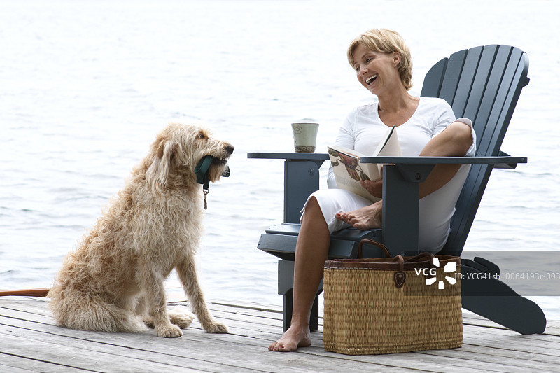 中年妇女坐在湖边的椅子上看着狗，笑着图片素材
