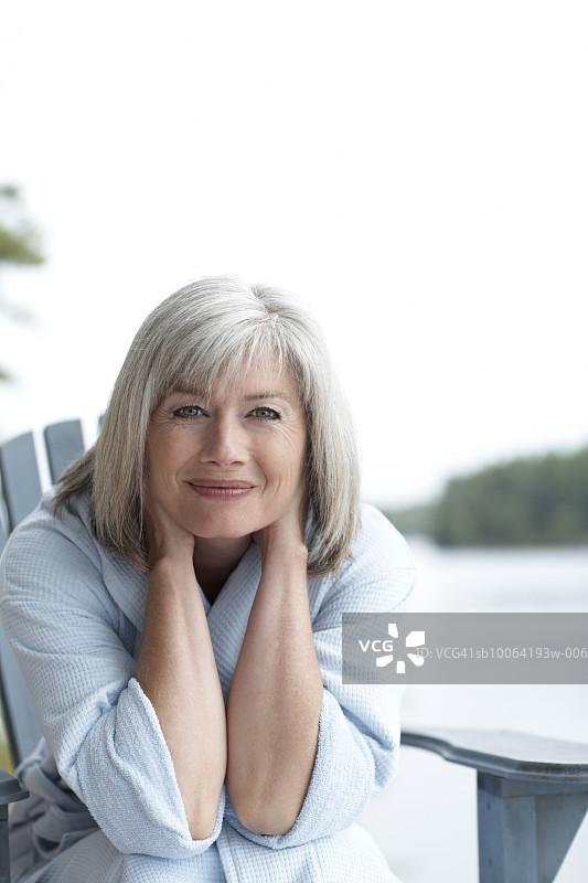 坐在椅子上，手放在头发上微笑的中年妇女肖像图片素材