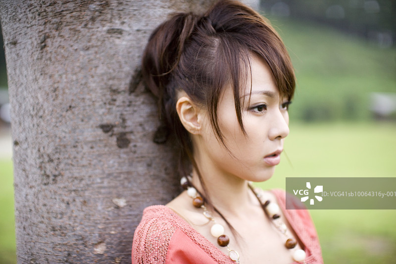 年轻女人倚靠在树上，特写图片素材