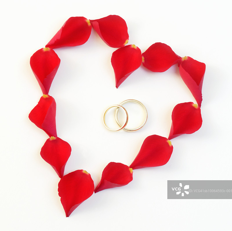 用红色玫瑰花瓣制成的心形，两枚结婚戒指置于其中，特写图片素材